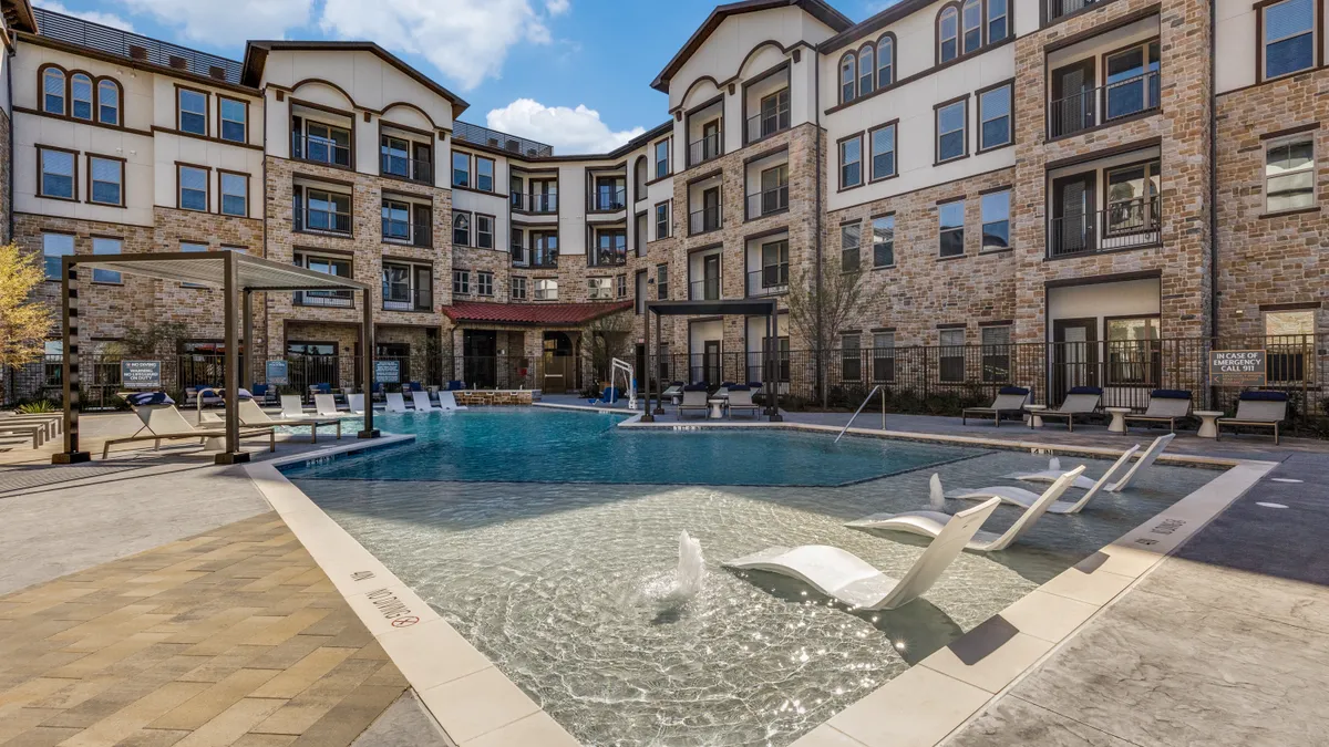 Four-story brown apartment building with a pool on the foreground.