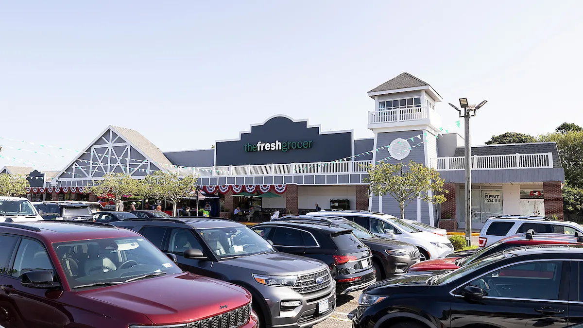 Exterior of The Fresh Grocer supermarket with full parking lot in front of it.