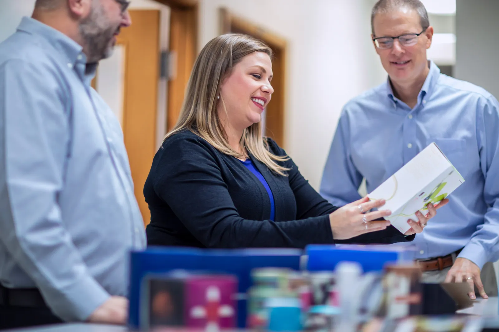 Three people stand in a technology center holding and looking down at packaging samples.