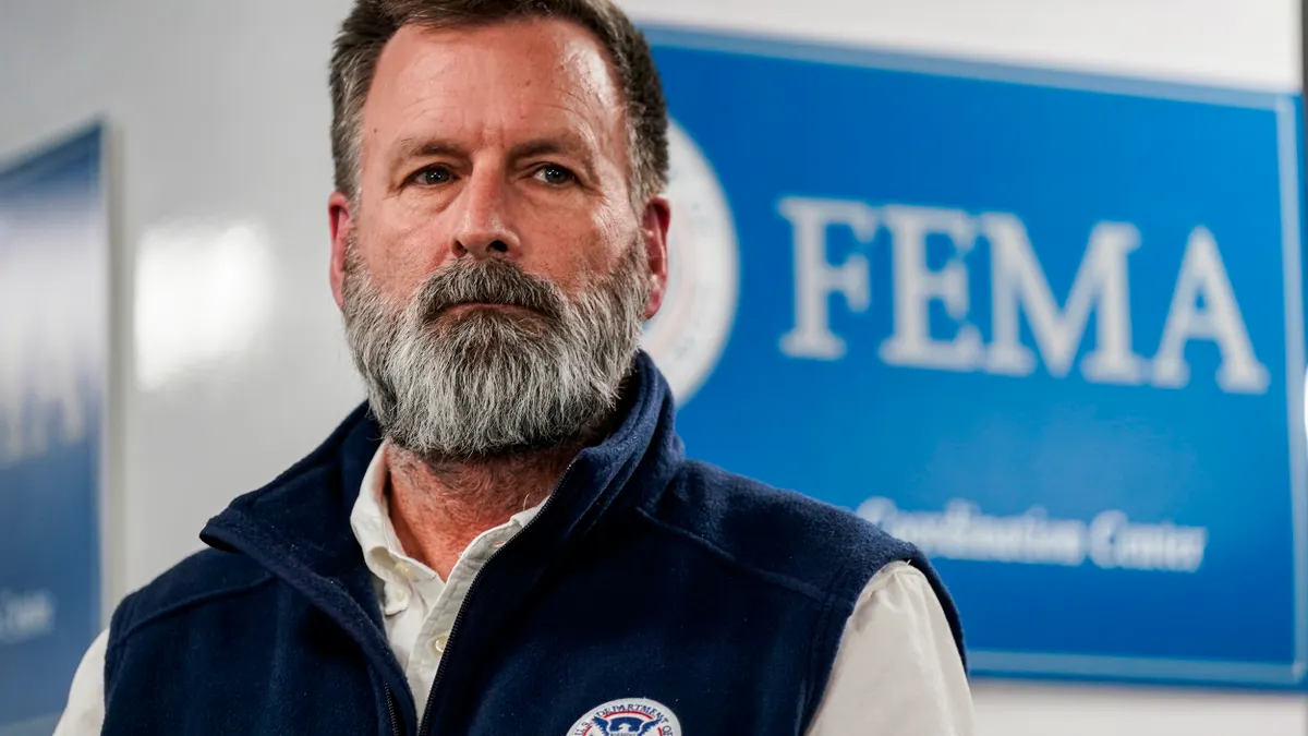 A person with a beard in front of a sign that says FEMA.