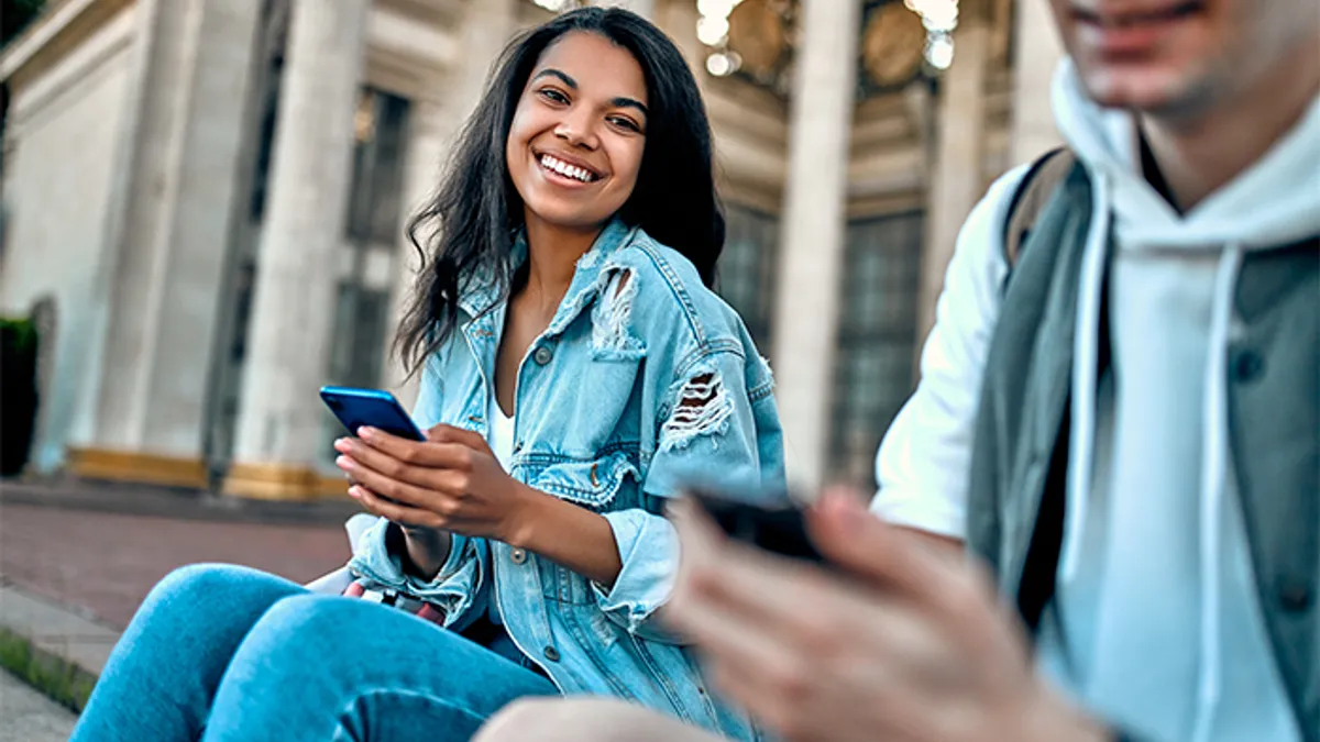 Girl and boy sitting together smiling with cellphones in hand.