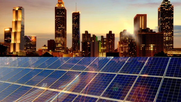 A commercial building bears rooftop solar panels facing the twilit skyline of Atlanta, Georgia