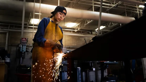 A person uses a torch cutter with a backwards hat in a manufacturing facility