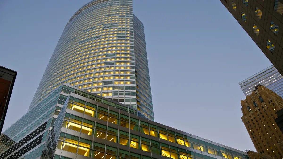 A cityscape photographed at dusk, featuring the global headquarters of Goldman Sachs Company in center left, set in contrast to older buildings along New York's financial district.