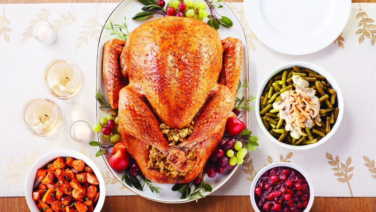 Overhead picture of a table with a cooked turkey in the center and three separate bowls surrounding it holding various side dishes