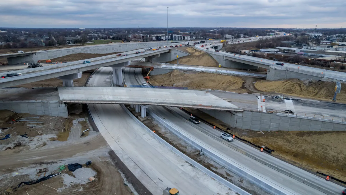 Multiple lanes of highway cross over each other, with a newly poured bridge and construction equipment in the foreground.