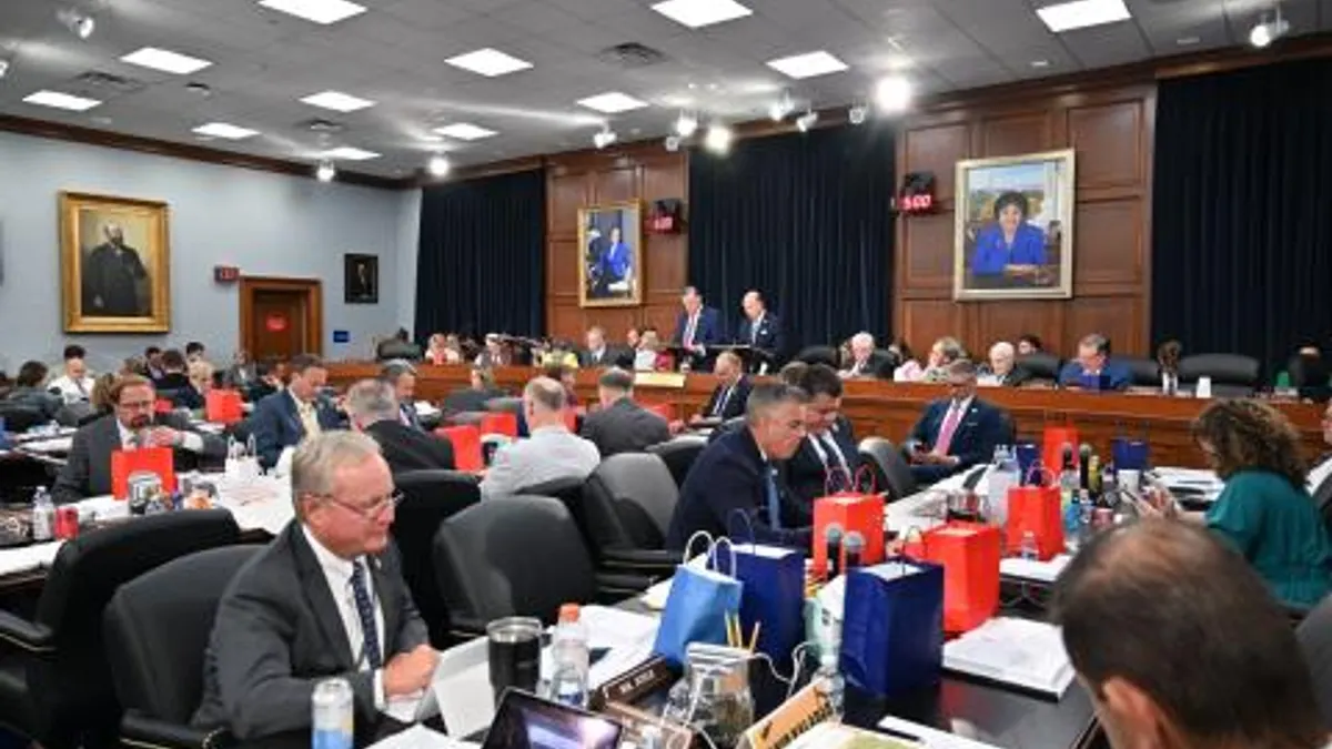 A room full of people are sitting at tables and looking at papers and computers on the tables.