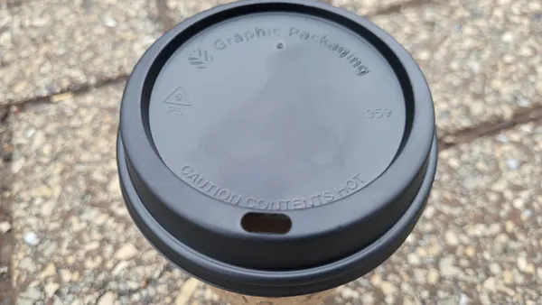 A close-up view of a black hot cup lid with Graphic Packaging International's name and a symbol indicating polystyrene.