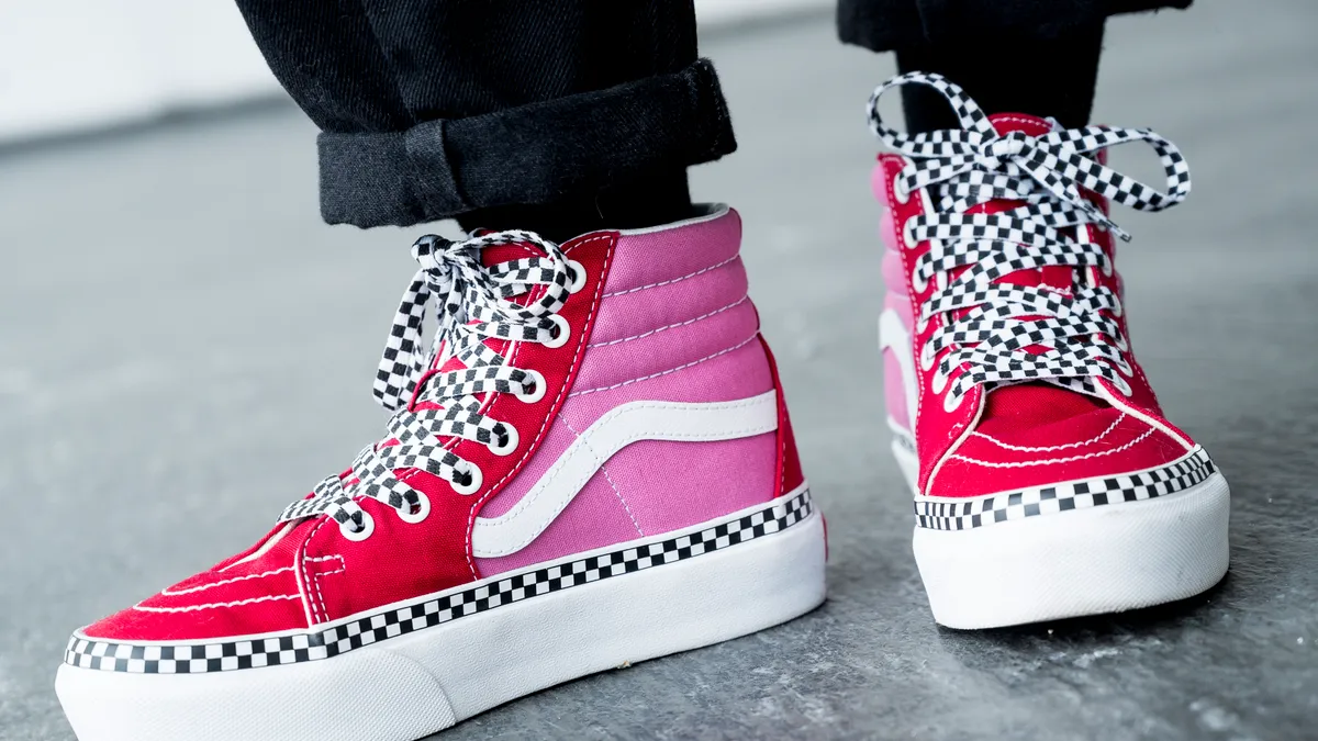 A closeup of a person's shoes, pink and red Vans with checkered shoelaces.