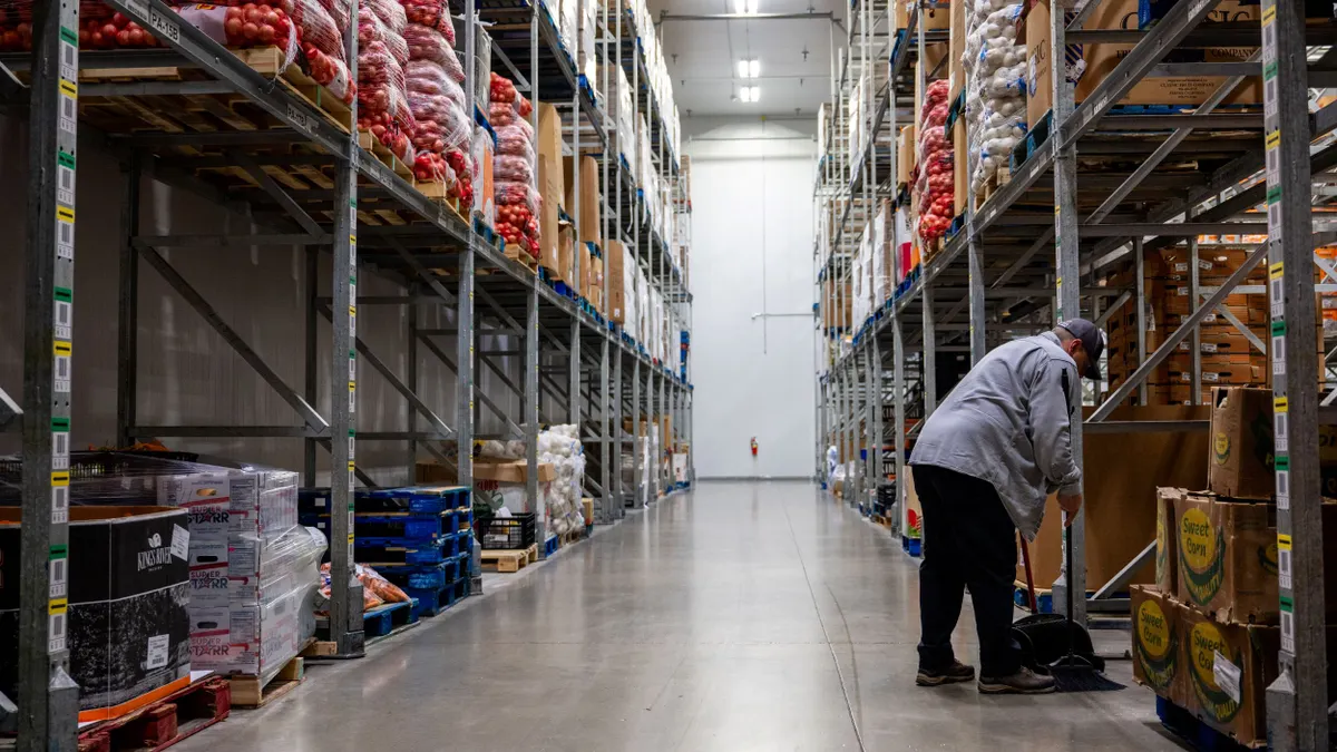 A lone employee cleans in a warehouse aisle.
