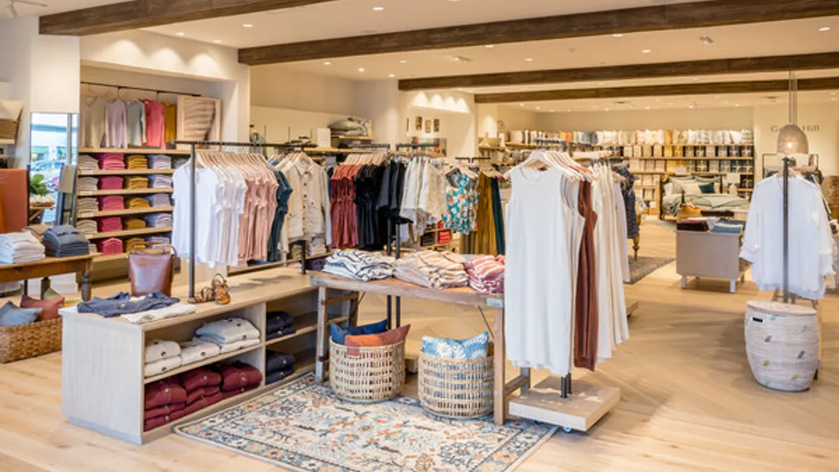 The interior of a clothing store, with racks of dresses and shirts, and shelves with folded garments.