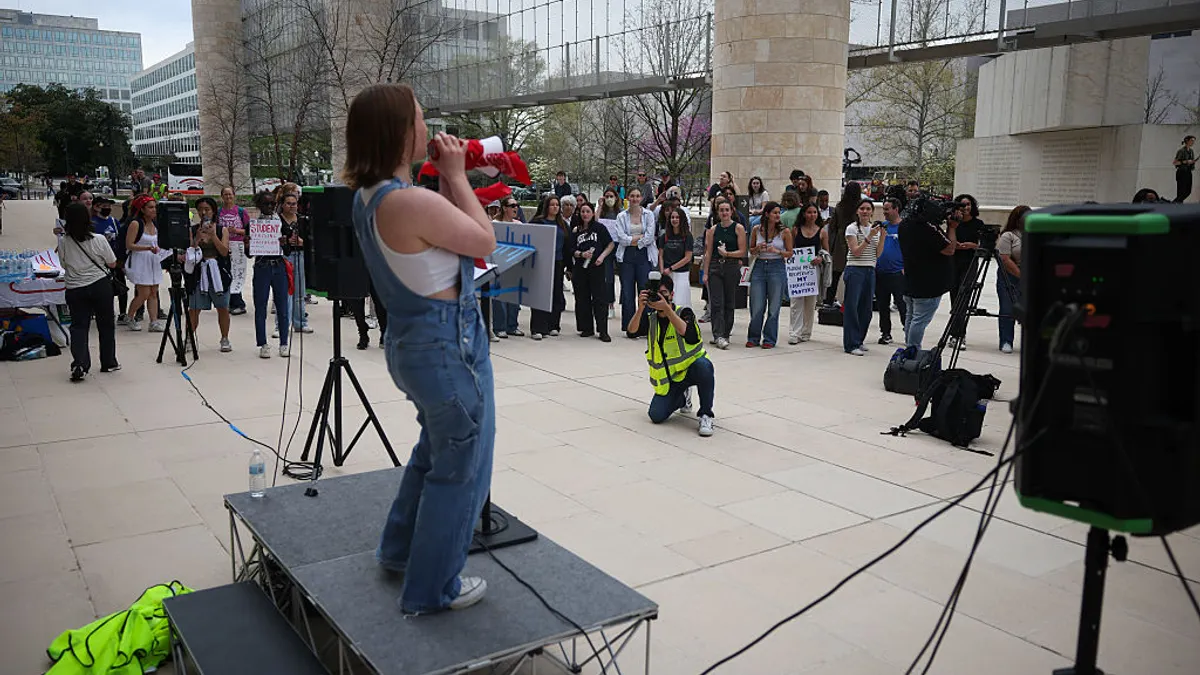Students gather to protest outside the U.S. Department of Education headquarters. One student is in the center and has a megaphone.