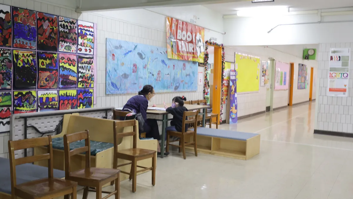 A Pre-K student sits with a teacher outside a classroom at Yung Wing School P.S. 124 on March 07, 2022 in New York City.