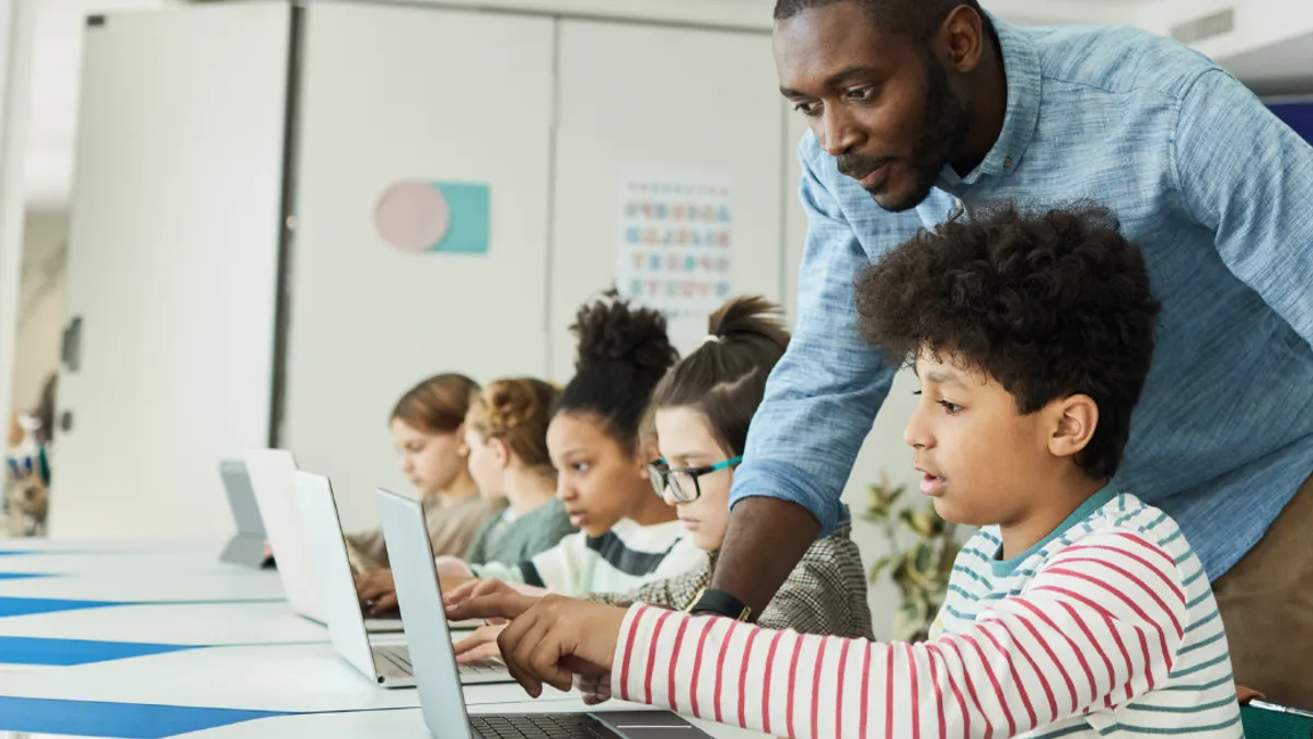 Teacher helping a student study on a laptop.