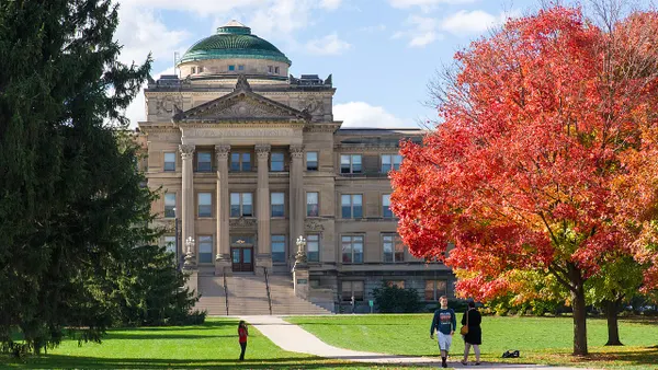 Sparsely spaced pedestrians on quad green in fall in front of classical building.