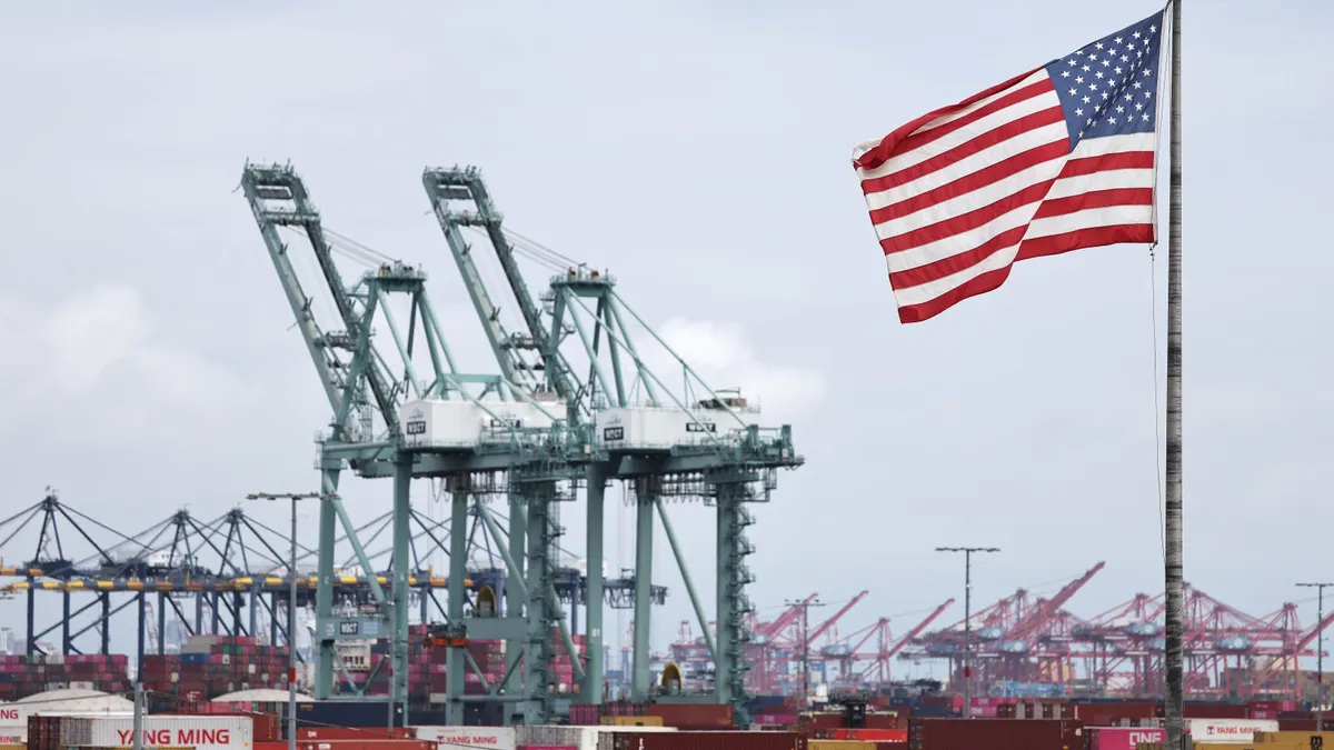 A U.S. flag flies in front of shipping containers and cranes at the Port of Los Angeles on Sept. 26, 2025.