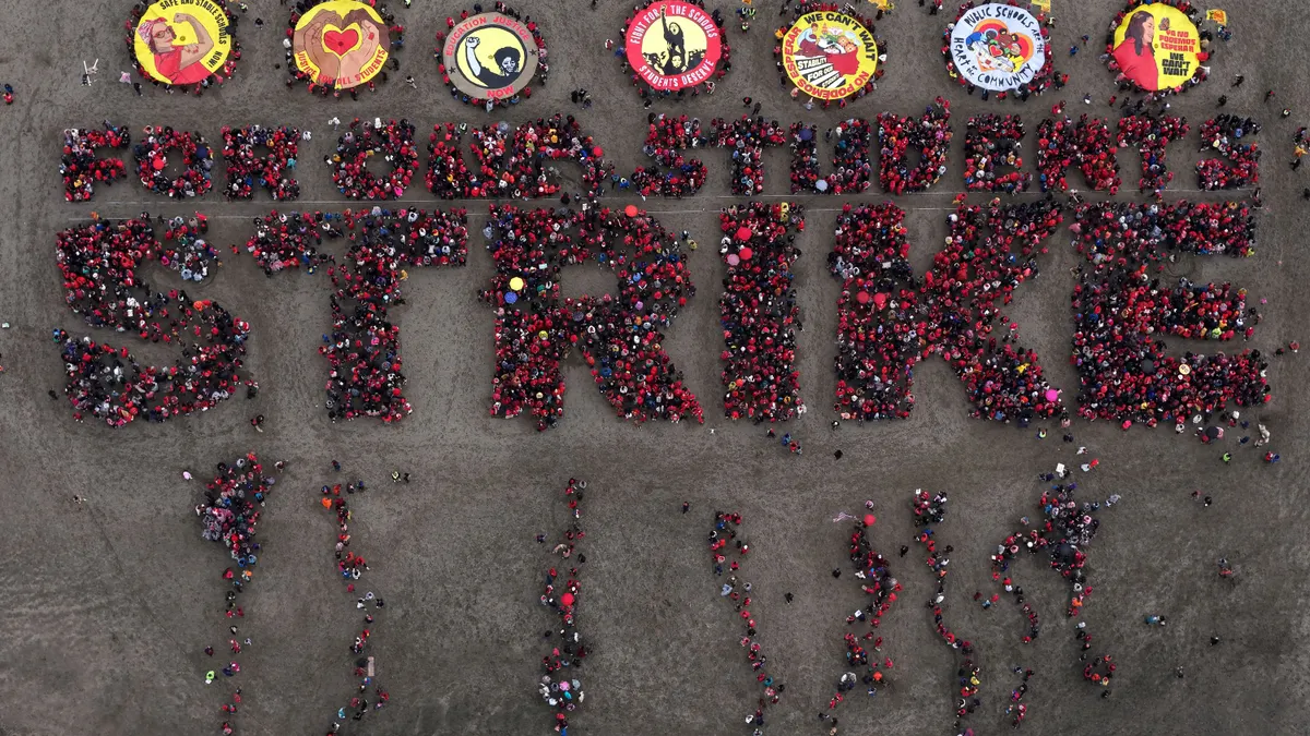 An aerial view shows protesters dressed in red spelling standing in formation to spell out "For our students, strike" on a beach.