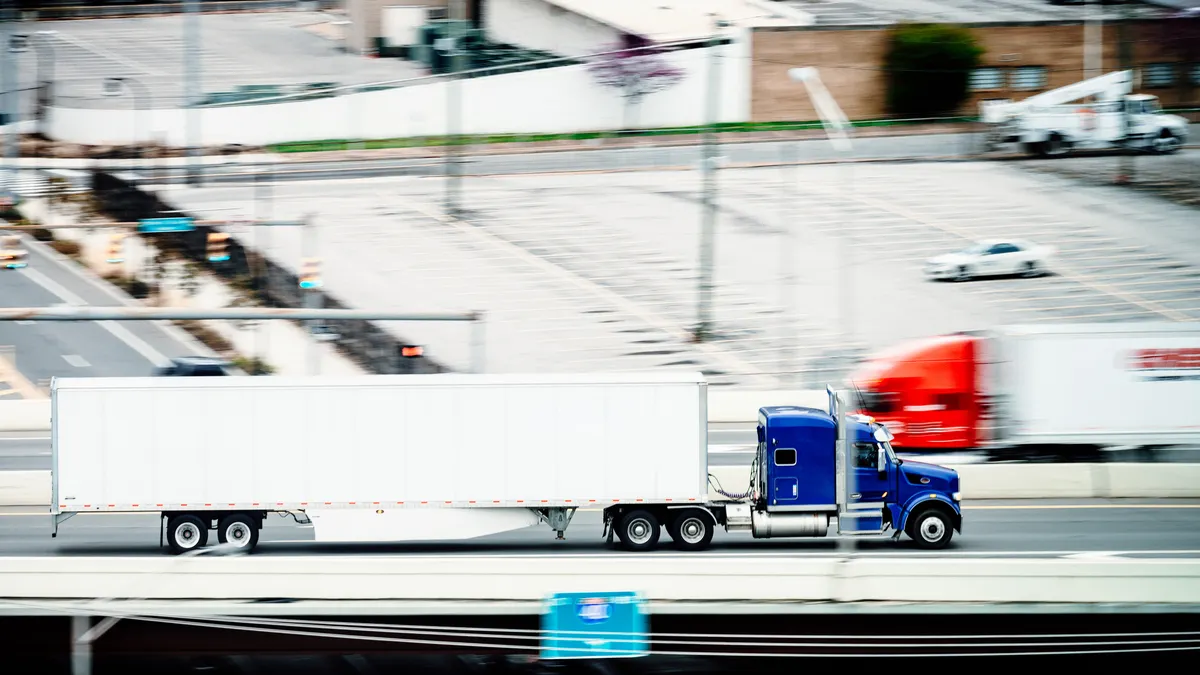 A blurred photo captures the speed of two trucks going opposite ways on a highway with a parking lot in the background.