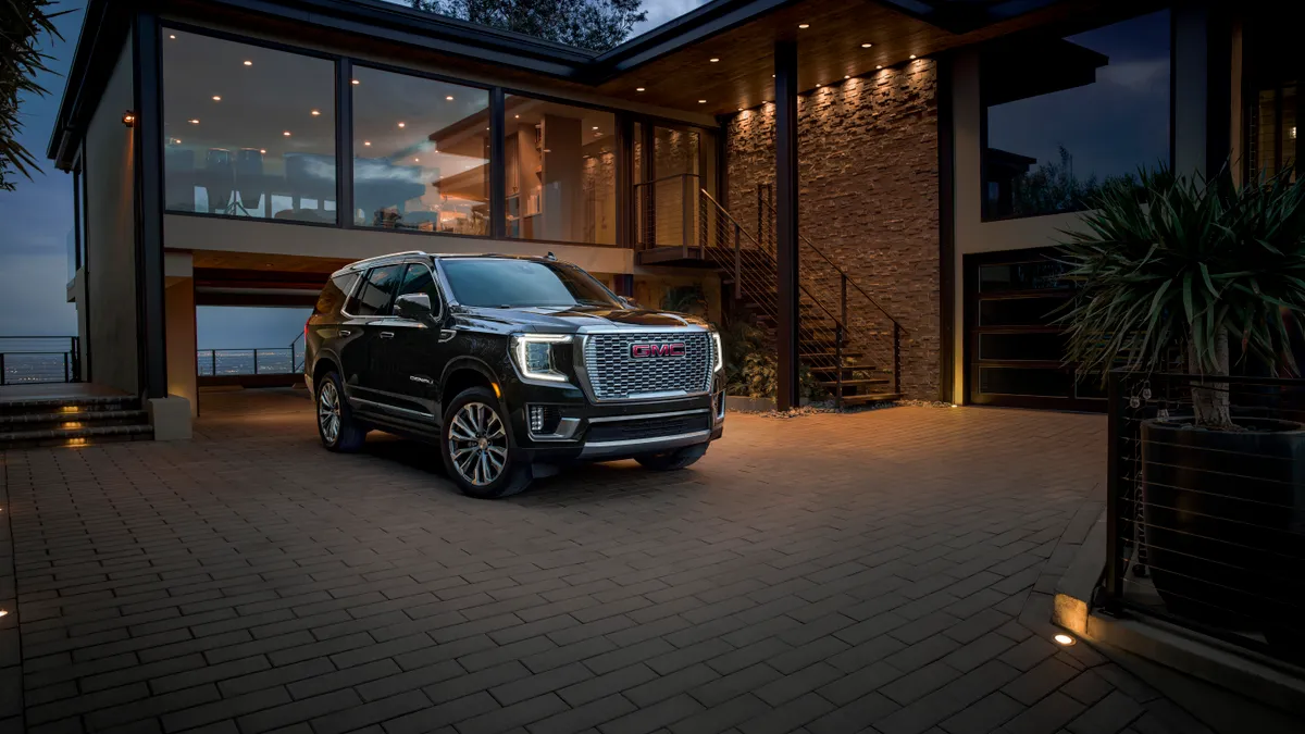 A black 2023 GMC Yukon Denali SUV parked in front of a house.