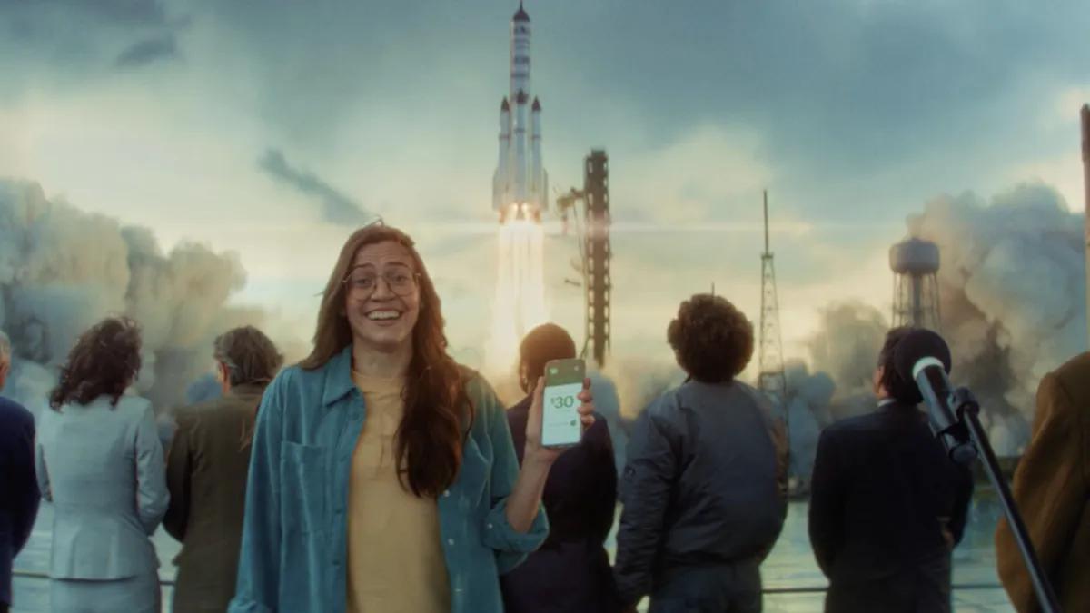 A young woman holds a phone in front of a space launch for a TD Bank ad