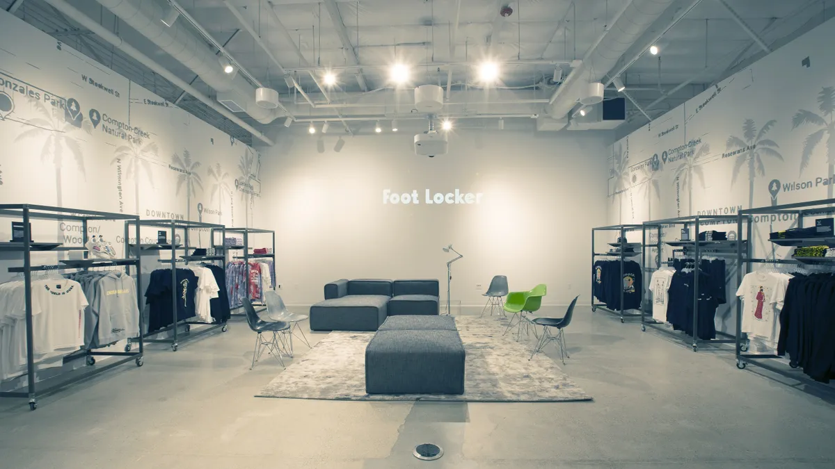 Comfortable seating on a rug in the middle of a sparsely merchandised Foot Locker store, where the interior is dominated by muted grays.