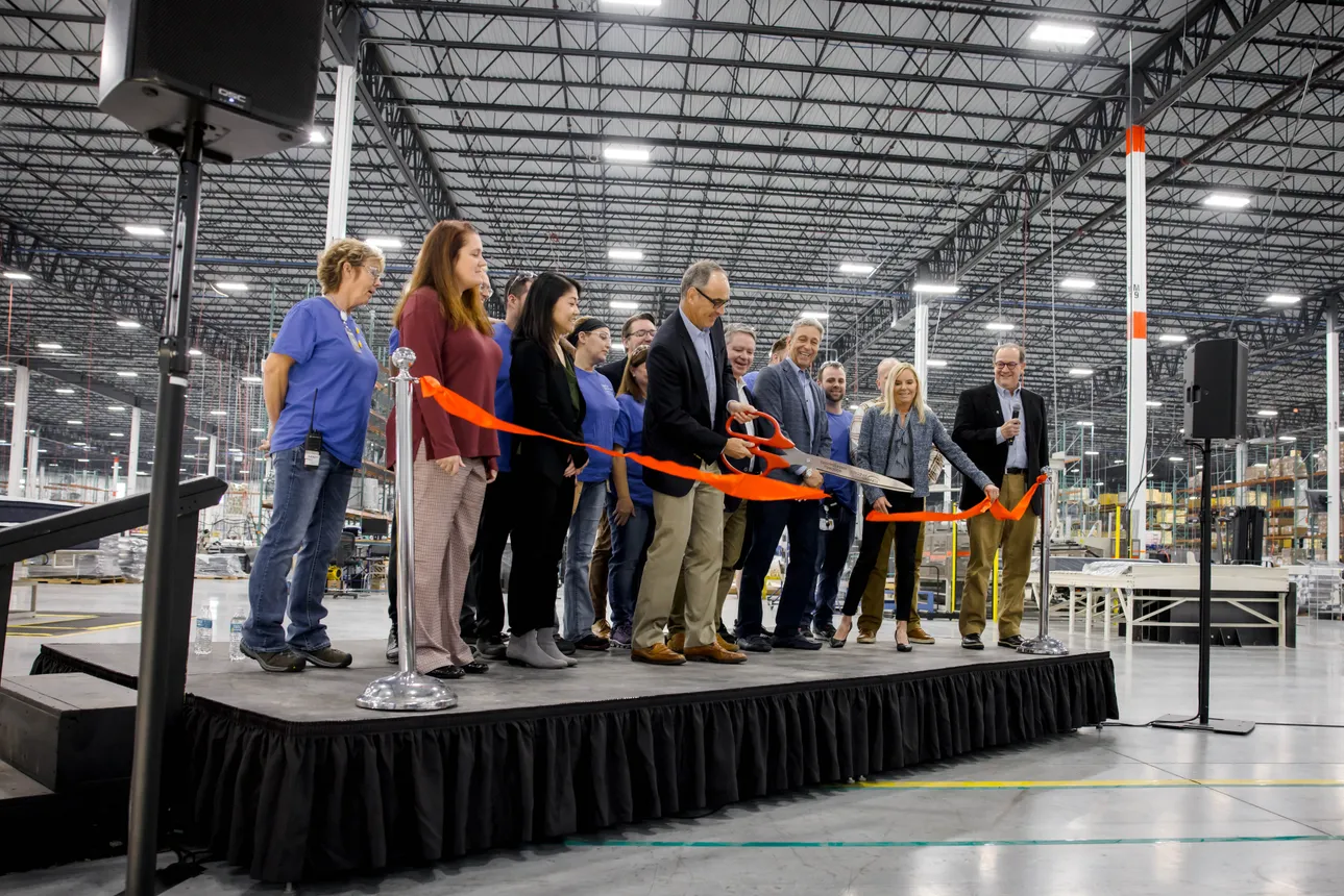 Person cutting a ribbon during a plant opening ceremony.