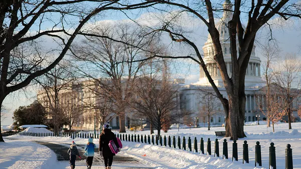 Two children and adult walk on a street near the U.S. Capitol building. There is snow on the ground and the adult is holding a sled.