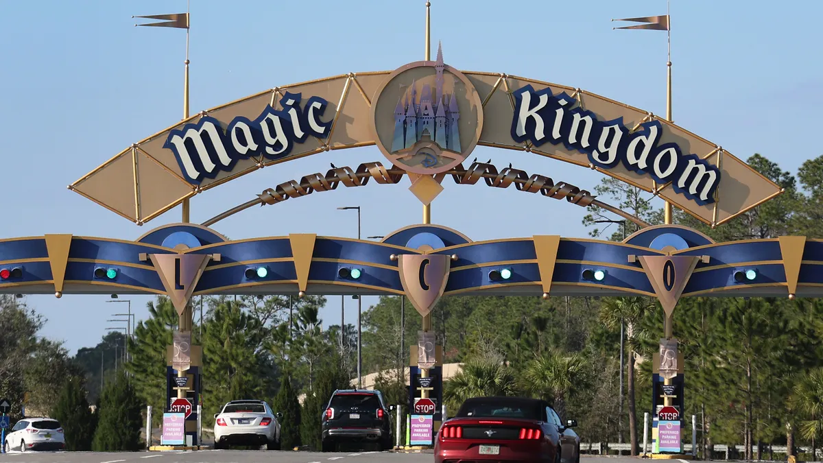 Cars pull up to a gate with a "Magic Kingdom" sign overhead.