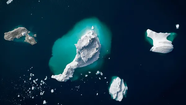 Aerial view of icebergs floating in dark blue ocean water beside a rocky landmass