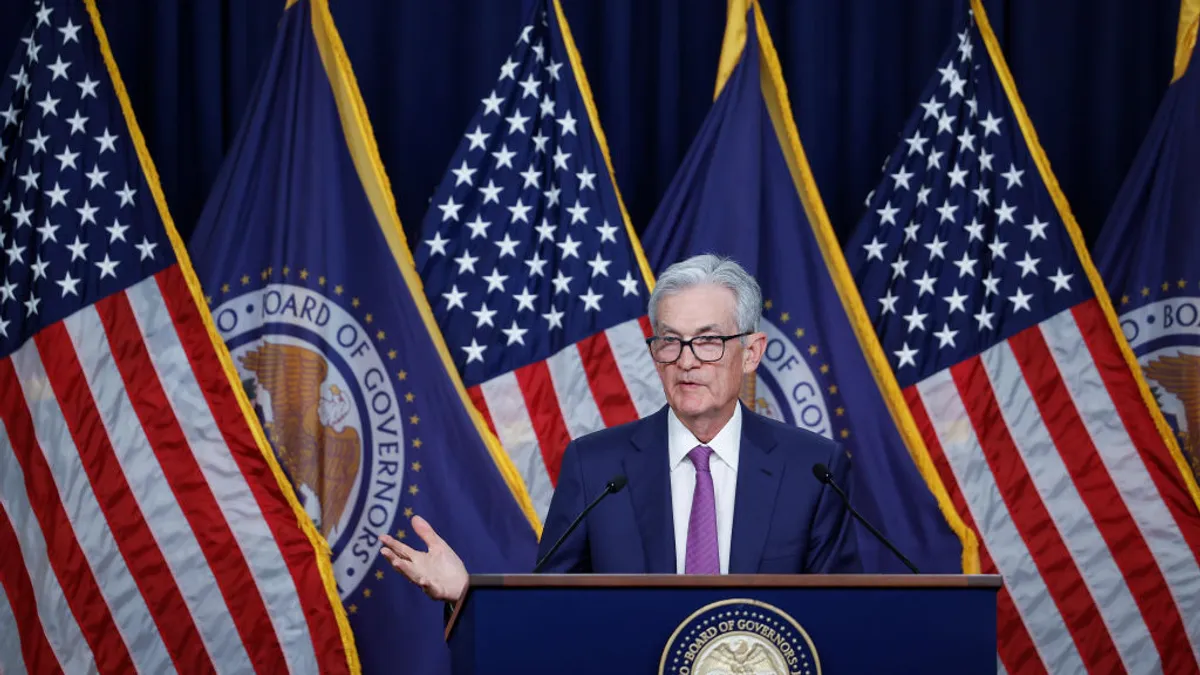 A man with silver hair in a suit gestures at a podium.