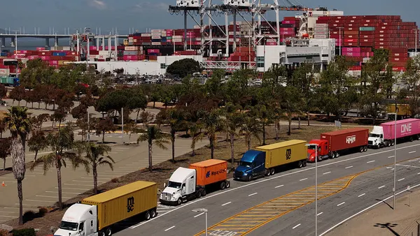 A line of trucks down the road next to an ocean port.