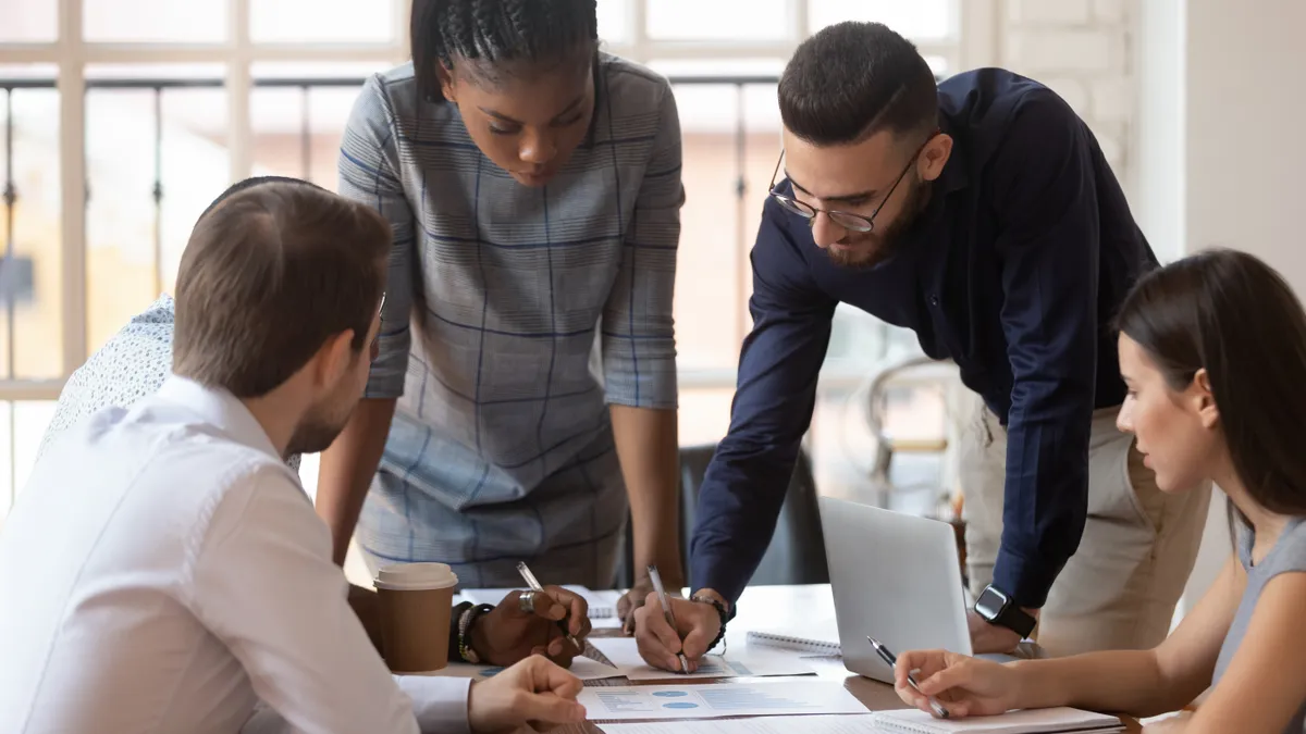 Four people bend over some documents on a desk in an office, making plans.