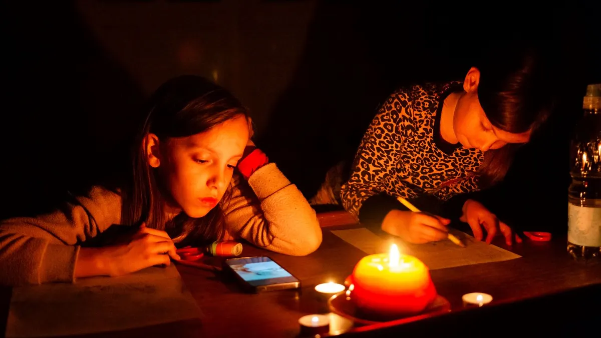 Two little girls draw on a table with a candle during a power outage
