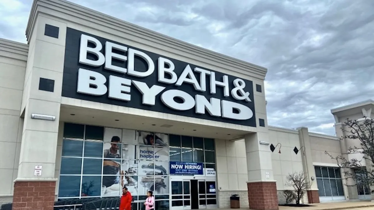 Two people walk by a Bed Bath & Beyond store on a cloudy day.