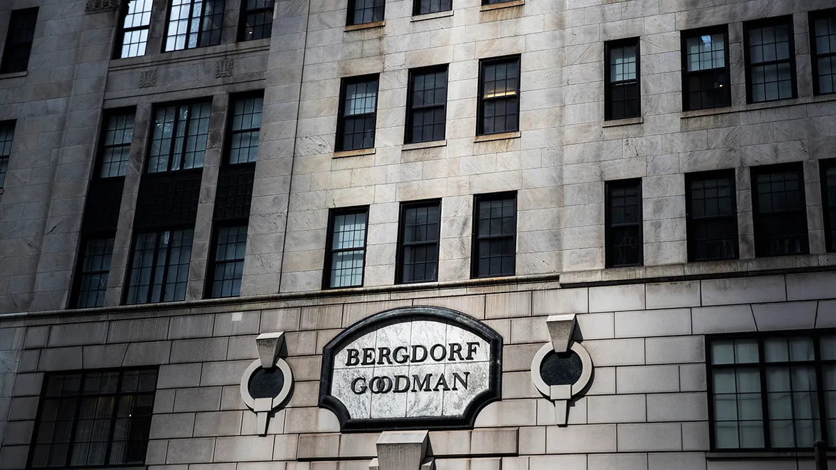 Sidewalk pedestrians walk past a storefront with large gold letters reading BERGDORF GOODMAN