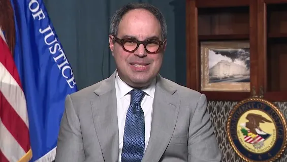 assistant US AG Jonathan Kanter sitting in front of the US flag and the DOJ seal