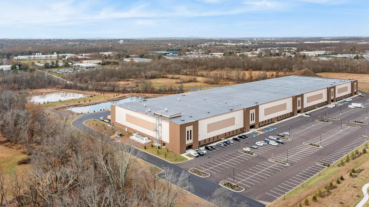 Aerial view of industrial plastics processing facility and parking lot, with rural landscape in background