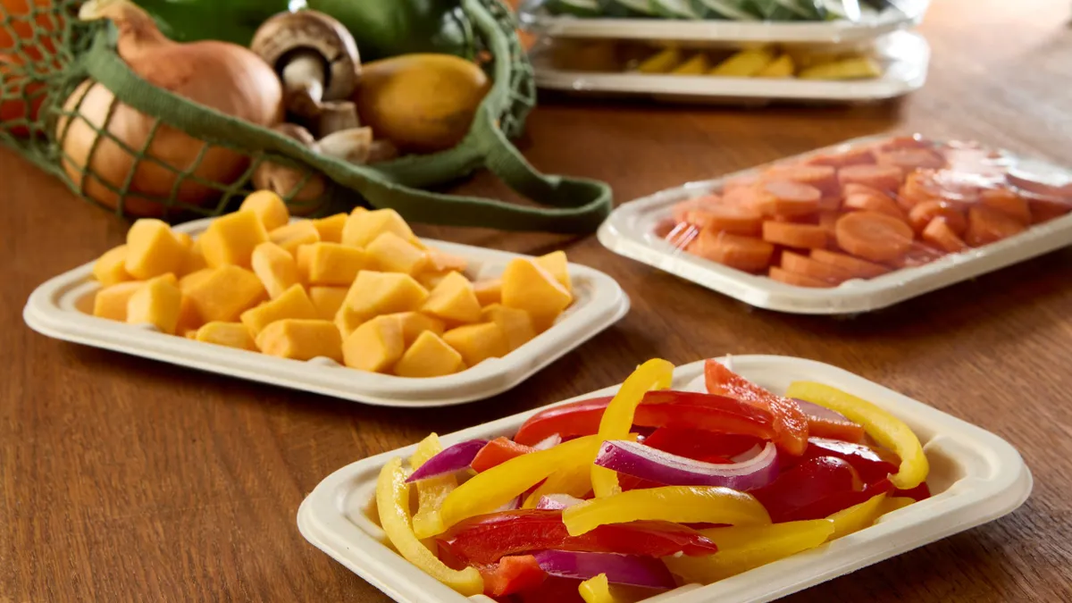 Three compostable Sabert trays with chopped vegetables on a table