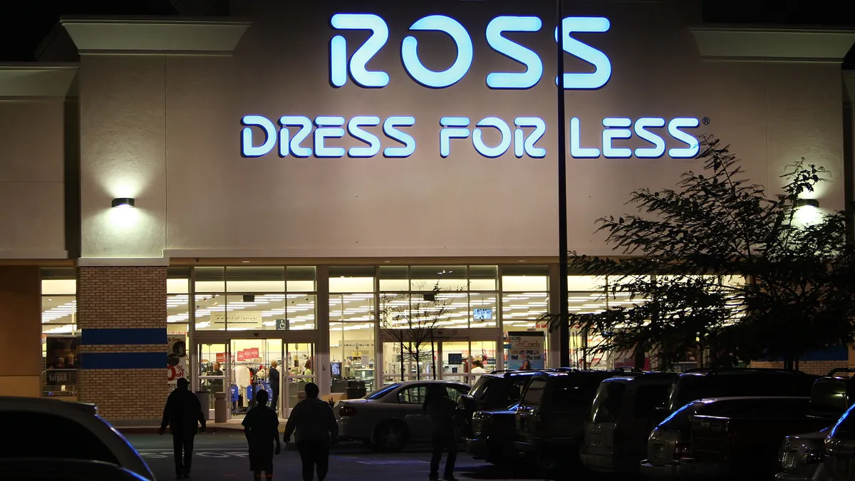 A Ross Dress for Less Storefront is shown at night, while customers walk towards it in the parking lot.