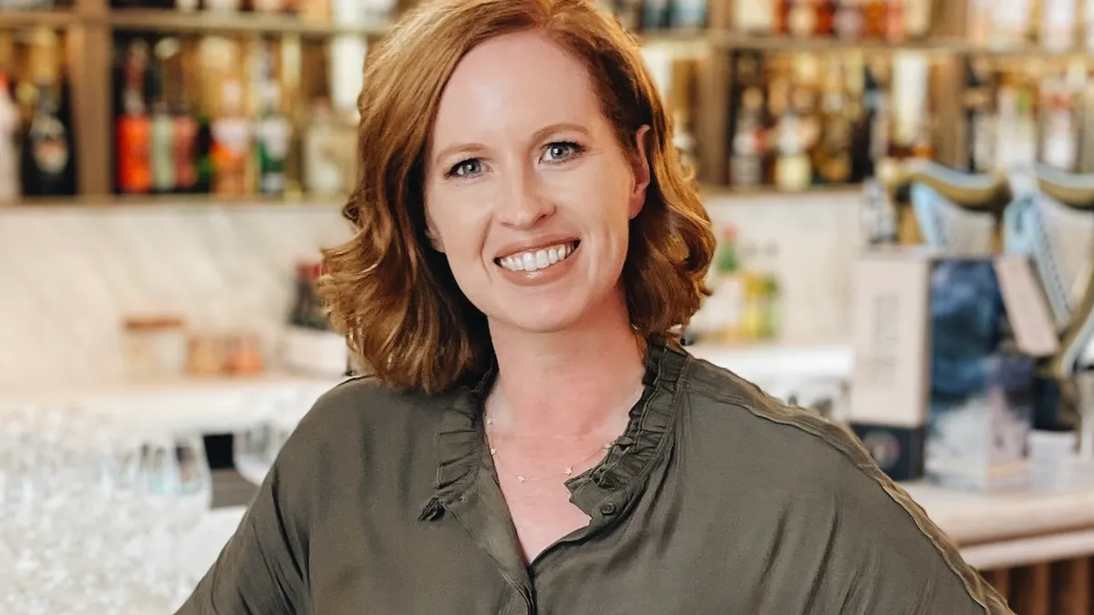 Janelle Orozco stands smiling in front of a bar.