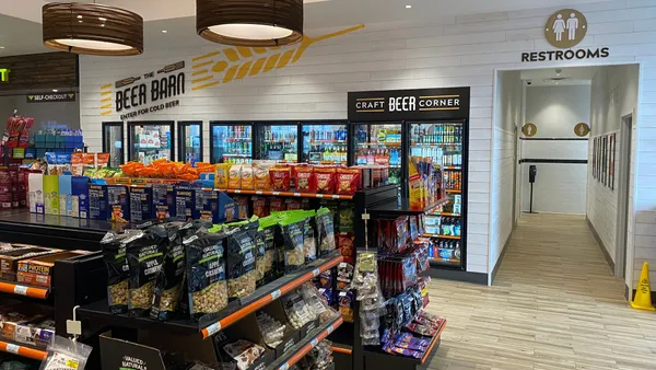 A photo of the interior of a convenience store, showing shelves full of snacks and a beer cave set in the back wall. Signs over the beer gave say "the beer barn. enter for cold beer." while a sign over a hallway to the right of the beer cave says "restrooms."