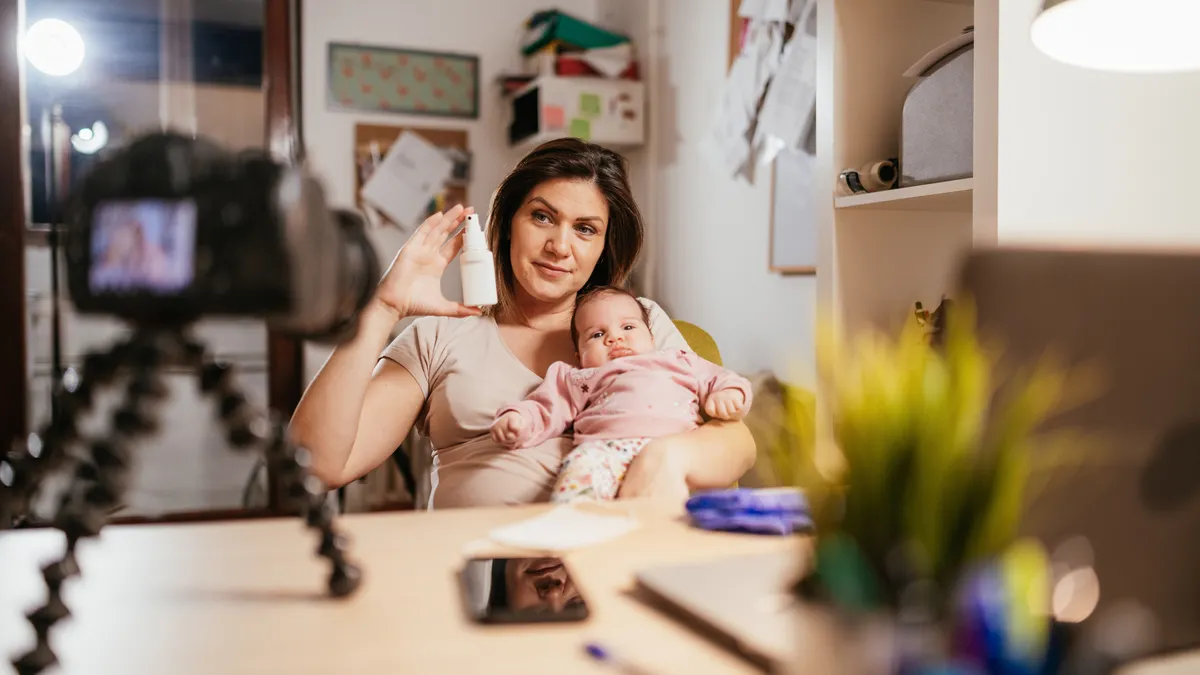 Adult woman vlogging while holding infant baby and a white spray bottle