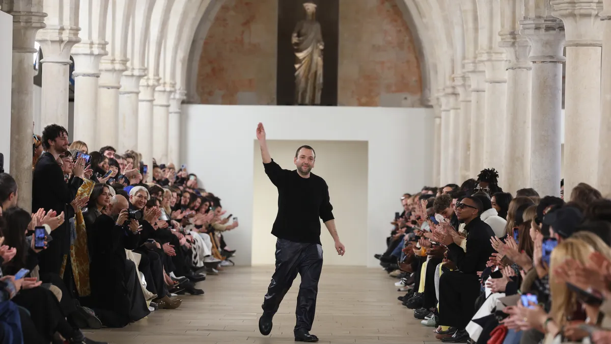 A man, designer Bruno Sialelli. stands at the end of an elaborate runway and waves goodbye to the crowd.