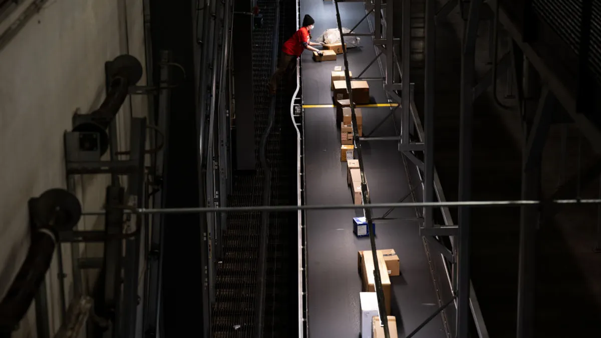 An employee removes packages from a moving conveyor belt in a loading area of a UPS facility.