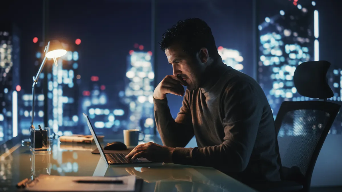 Thoughtful businessman working on laptop computer in a big city office at night.