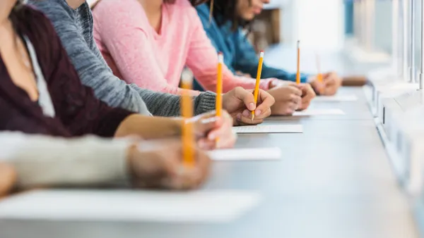 A row of students sit next to each other at their desks as they individually complete a standardized test.