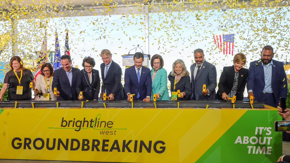 Large group of men and women at a table with confetti flying above them. Sign on table reads Brightline West.