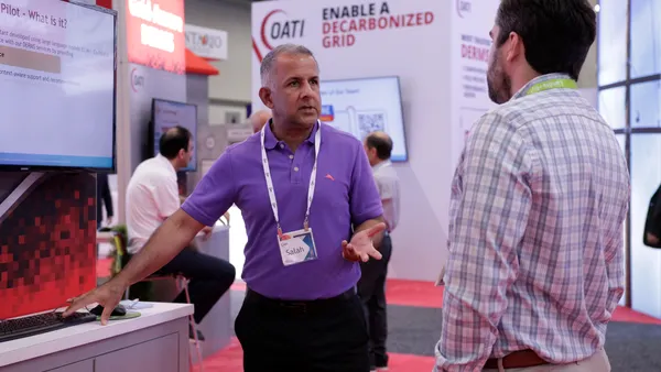 Two men engaged in conversation at a bustling trade show, surrounded by various booths and attendees.