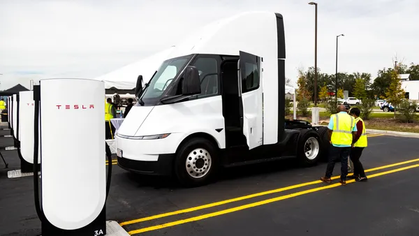 A Tesla Semi in a Megacharger stall with people nearby in high-visibility vests.