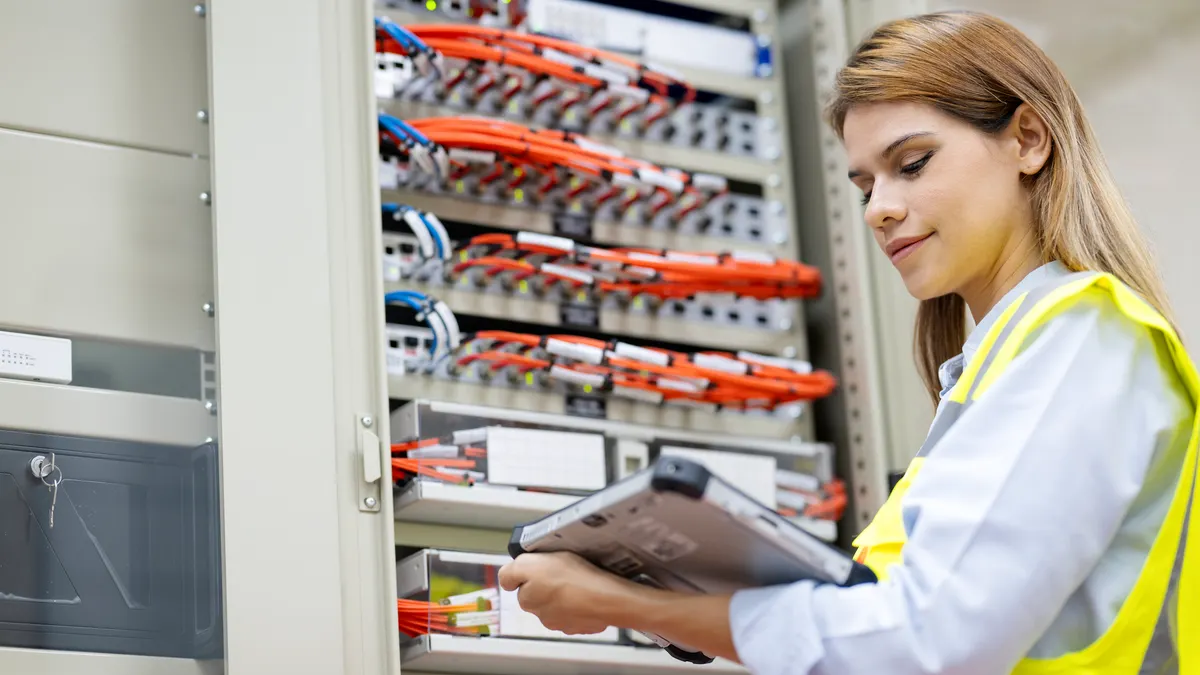 Improved Efficiency and Enhanced Data Protection of Business Operations with Data Center Solutions. A female Network engineer using a tablet computer to troubleshoot and network performance monitoring in a server room.